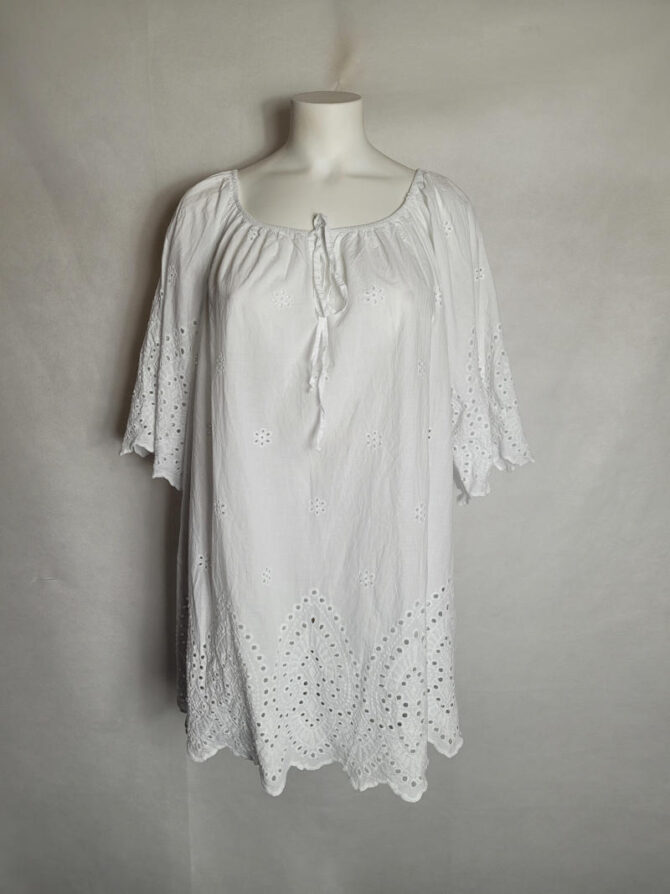 blouse blanche femme grande taille chic et original . Ce haut long de style bohème en coton blanc se distingue par sa broderie anglaise. Il se marie parfaitement avec des sandales et des accessoires, et sa coupe évasée est idéale pour la saison estivale. vetements grandes tailles chic​